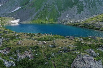 Aerial drone view of alone woman traveler in dress and hat watching on Seven colored mountain glacial lake, summer landscape: high peaks, snow, stones. Arkhyz, Caucasus, Karachay-Cherkessia, Russia