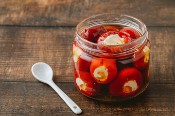 Stuffed cherry peppers with ricotta cheese filling in glass jar on wooden background