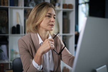 Attractive middle aged woman working at office, using contemporary desktop computer.