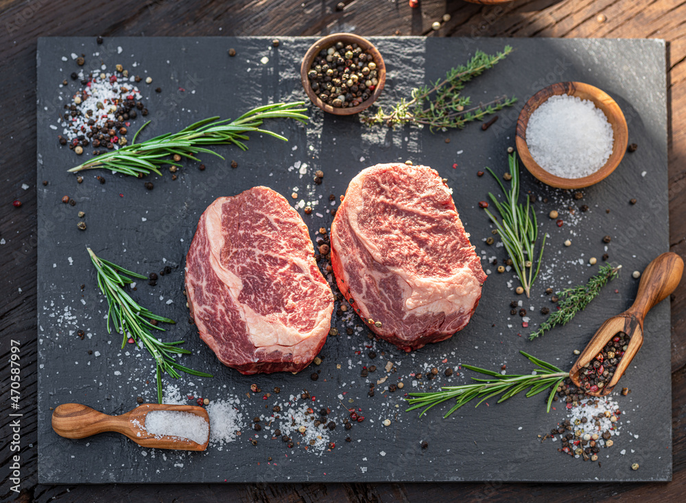 Wall mural Raw Ribeye steaks with salt and herbs on grey board. Top view.