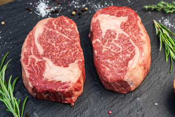 Raw Ribeye steaks with salt and herbs on grey board. Top view.