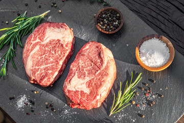 Raw Ribeye steaks with salt and herbs on grey board. Top view.