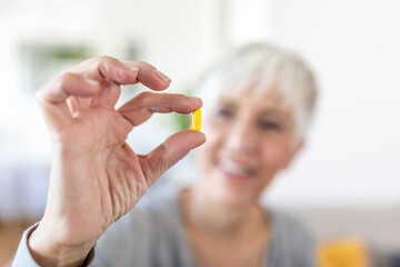 Senior woman at home sitting at table and kitchen at home holding cup of water and pill coronavirus treatment close-up blurred background