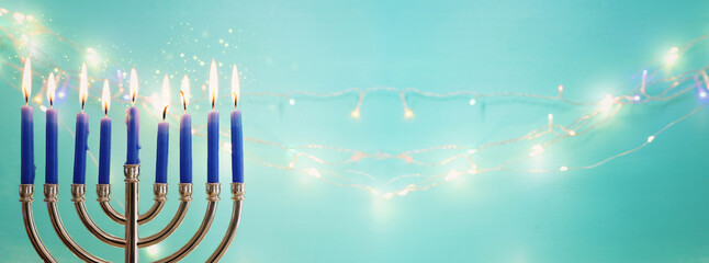 Image of jewish holiday Hanukkah with menorah (traditional candelabra) and candles over garland glitter lights background