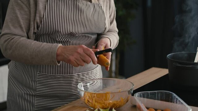 Detail of caucasian senior woman peeling a carrot while cooking in the kitchen. Shot with RED helium camera in 8K   