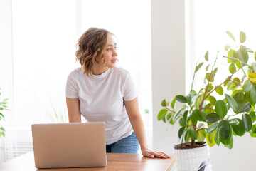Business woman using laptop standing near desk white office interior with houseplant looking a side