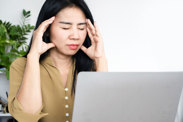 stressed Asian woman having headache, migraine at work tired from working on computer hand touching...