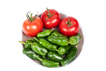 Green peppers and red tomatoes on a plate on a white background. Vegetarian food concept