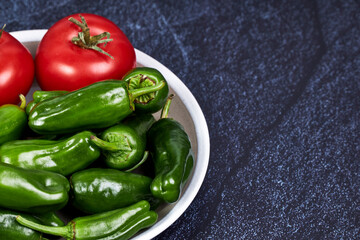 Green peppers and red tomatoes on a plate on a piece of slate. Healthy food concept