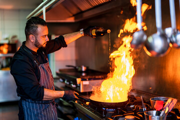 Chef preparing flambe dish on stove in restaurant kitchen