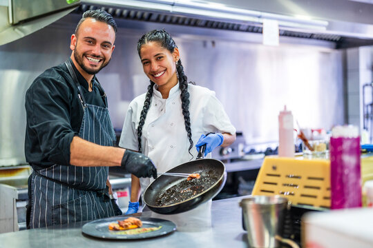 Smiling Kitchen Assistant Helping Chef In Preparing Food In Restaurant