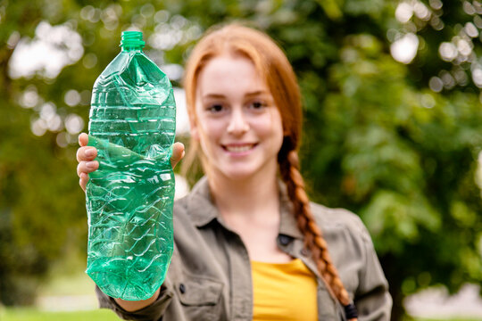 Smiling female environmentalist showing plastic bottle in garden - Powered by Adobe