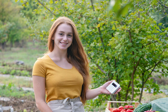 Smiling female farmer holding credit card reader in garden