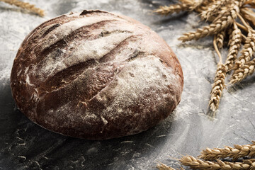 Fresh bread on a table close-up in a sprinkling of flour and wheat ears, selective focus. Healthy...
