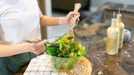 salad concept the woman with white t-shirt and dark green pants standing at the kitchen and making a bowl of green salad