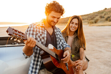 White man playing guitar during travel on car with his girlfriend