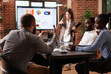 Businesswoman discussing project ideas pointing at monitor explaining company strategy working at financial presentation in startup office. Diverse businessteam planning business partnership