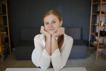 Fototapeta premium Young smiling successful business woman employee in white shirt smiling and looking at camera, sitting at white desk workplace with laptop computer in modern office indoors. Career achievement concept