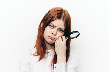 red-haired woman in a white shirt with a magnifying glass in her hands searching