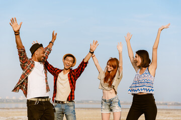Obraz premium Young multiracial friends laughing while posing with hands up