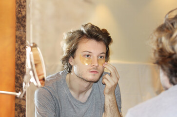 Fototapeta premium Anti-aging eye therapy. young man taking care of his undereye wrinkles applying facial mask. Dark Circles.Eye patches..