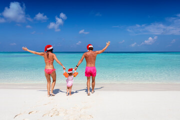 A happy family with santa claus hats runs into the turquoise sea of a tropical paradise beach...