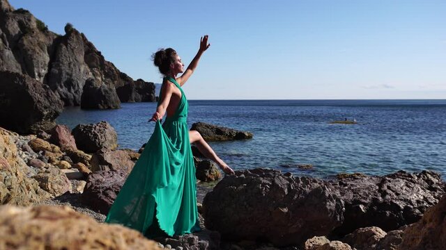 Side view a Young beautiful sensual woman with black hair in a long mint dress posing on a beach with calm sea bokeh lights on sunny day. Girl on the nature on blue sky background. Fashion photo