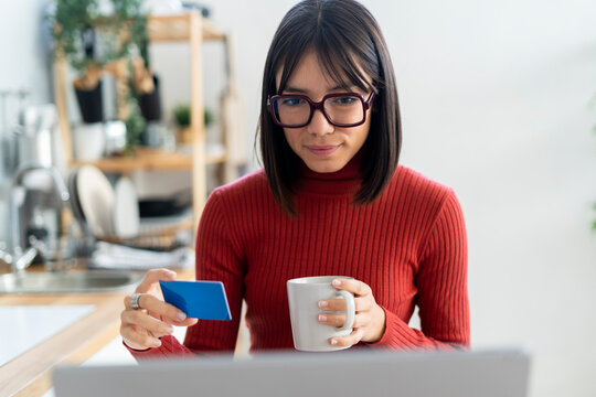 Freelancer with credit card holding coffee mug looking at laptop