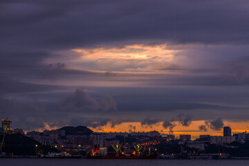 Naklejka na ściany i meble Vladivostok's marine facade during bright Dawn. Commercial port with industrial ships in a large sea city.