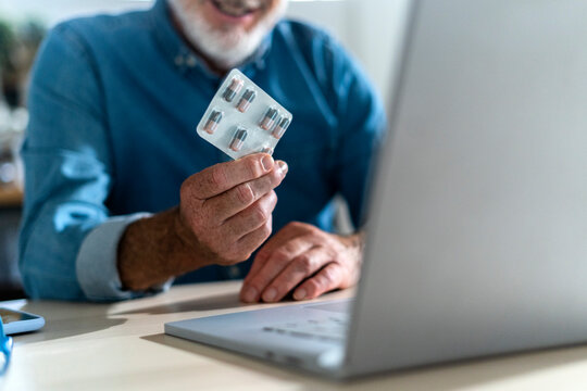 Senior man showing blister pack on video call with doctor
