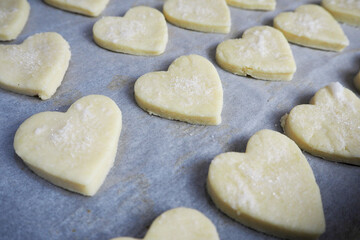 a lot of raw cottage cheese cookies are spread on parchment paper before baking on the side . baking at home for Valentine's Day