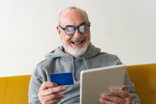 Bearded senior man doing online shopping through tablet PC at home