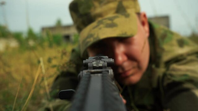 male soldier aiming from a machine gun while sitting in ambush