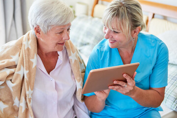 Krankenschwester hilft Seniorin beim Videochat am Tablet