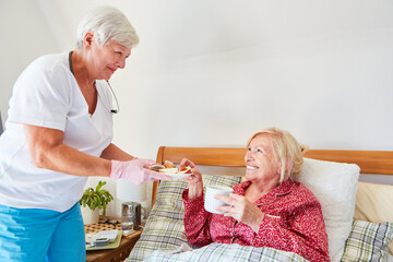 Fototapeta na wymiar Altenpflegerin bringt Frühstück ans Bett einer Seniorin