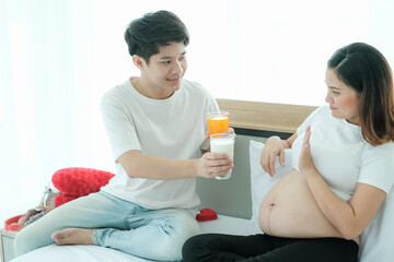 Obraz na płótnie Canvas Asian man take care pregnant woman and drinking milk