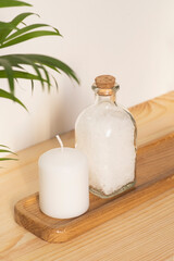 Fototapeta na wymiar Bottle filled with white bath sea salt and candle on natural wooden background. Beauty treatment for spa and wellness. Skincare natural cosmetic concept for body care.