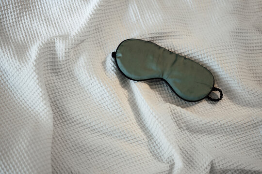 Silk Green Eye Mask Lying On The White Bedding In The Morning, Top View. Sleeping Concept.