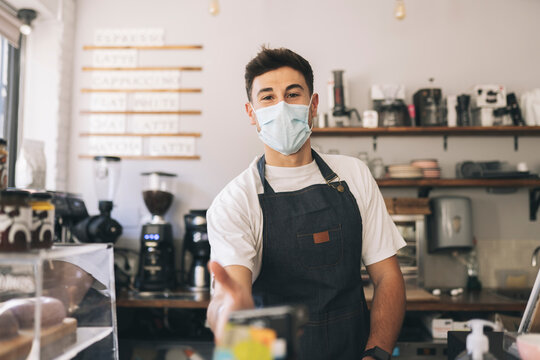 Cashier with protective face mask holding credit card reader in cafe