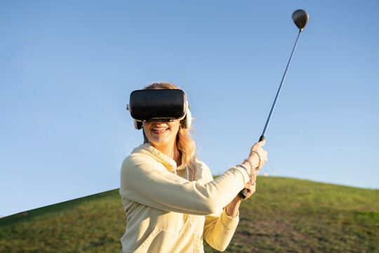 Smiling woman with gold club using virtual reality headset on hill