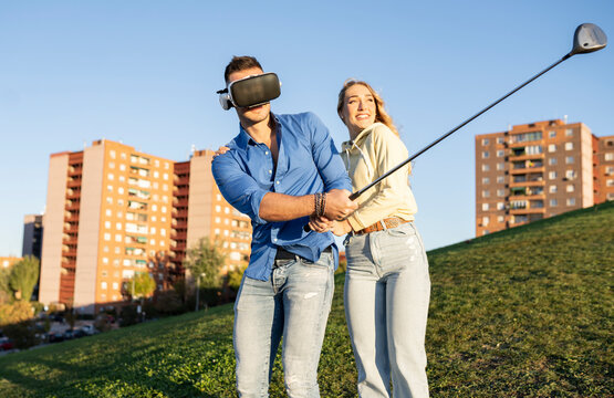 Man with virtual reality headset playing golf by girlfriend on hill