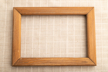Wooden frame on smooth white linen tissue. Top view, natural textile background.