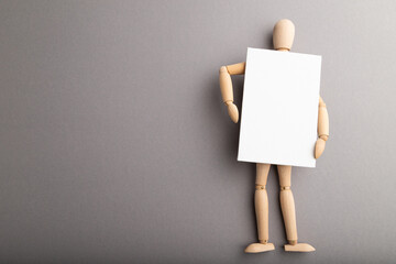 Wooden mannequin holding blank poster on gray pastel background. copy space.