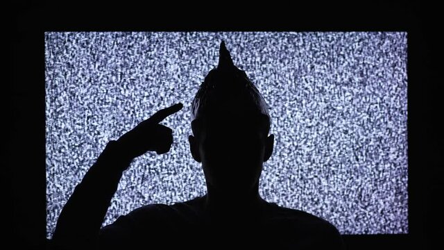Silhouette of a man wearing tin foil hat in a front of TV
