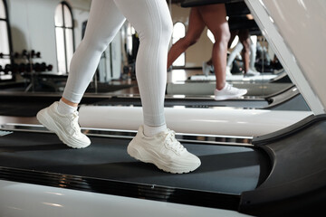 Woman in white leggins and sneakers running on treadmill in the morning