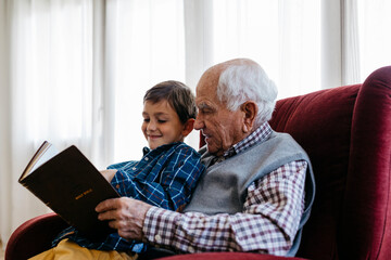 Grandfather reading bible with grandson at home