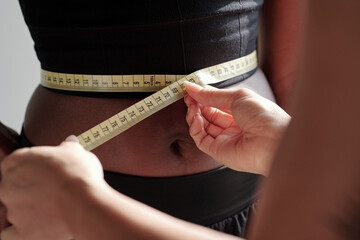 Close-up image of trainer measuring waist of her slim fit client before workout