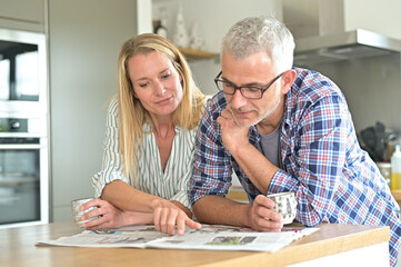 Middle-aged couple in kitchen reading newspaper