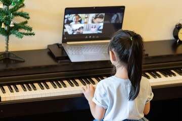 asian girl play piano online from   her laptop. backside of girl learning piano. Concept : home education for music lesson.