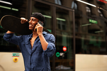 African man with skateboard. Young handsome man using the phone..